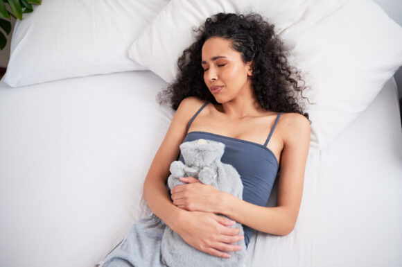 Eine multiethnischen Frau mit Wärmflasche auf dem Bett gegen Krämpfe und Schmerzen